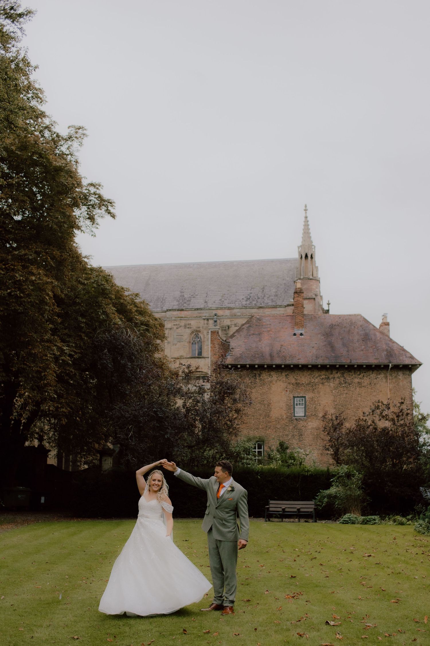 A couple dances playfully on the lawn of a historic stone church building.
