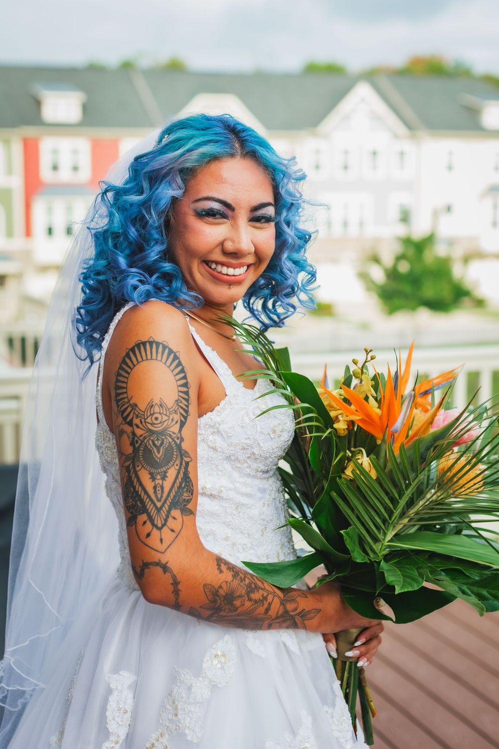 A bride with vibrant blue hair and intricate tattoos holds a tropical wedding bouquet.
