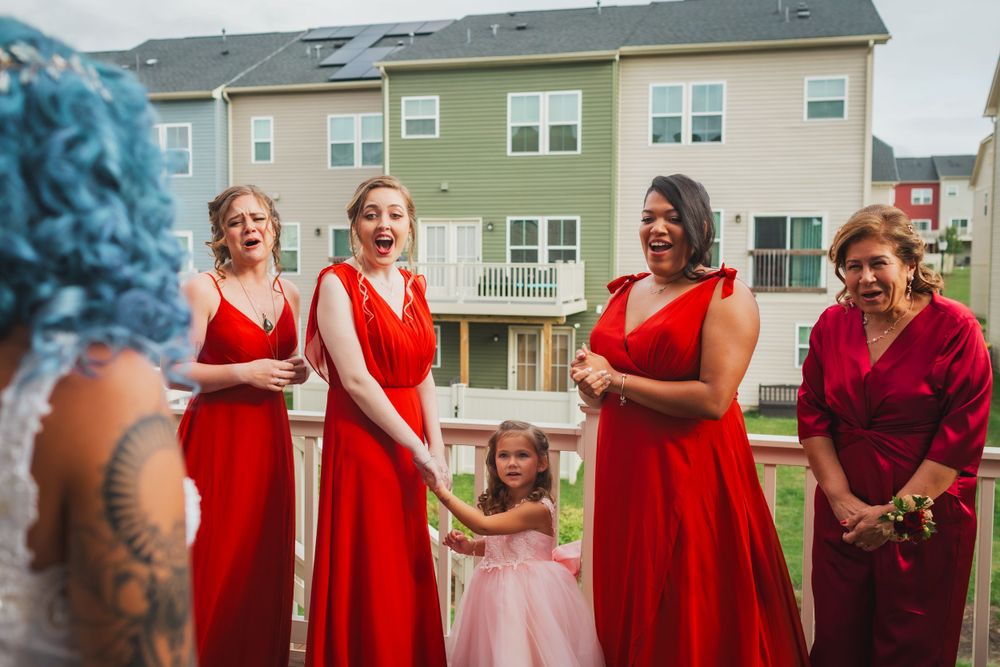 Bridesmaids in red dresses gather around a small flower girl in pink.