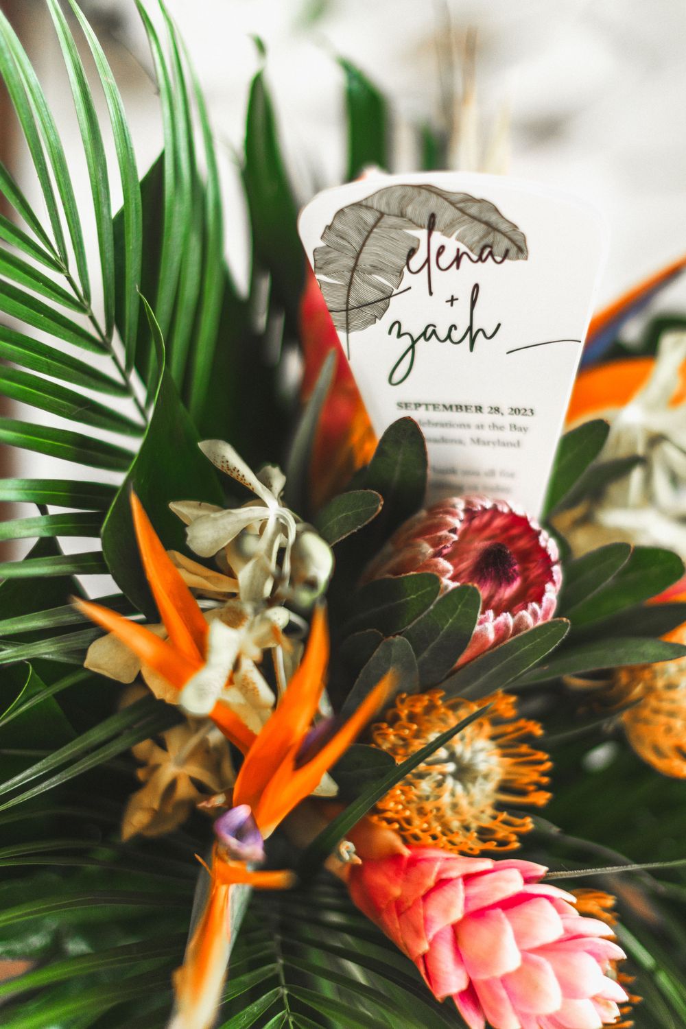 Wedding invitation nestled among tropical flowers and palm leaves.