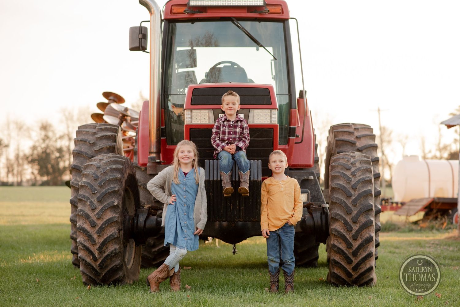 A family poses together on a large red farm tractor at sunset.