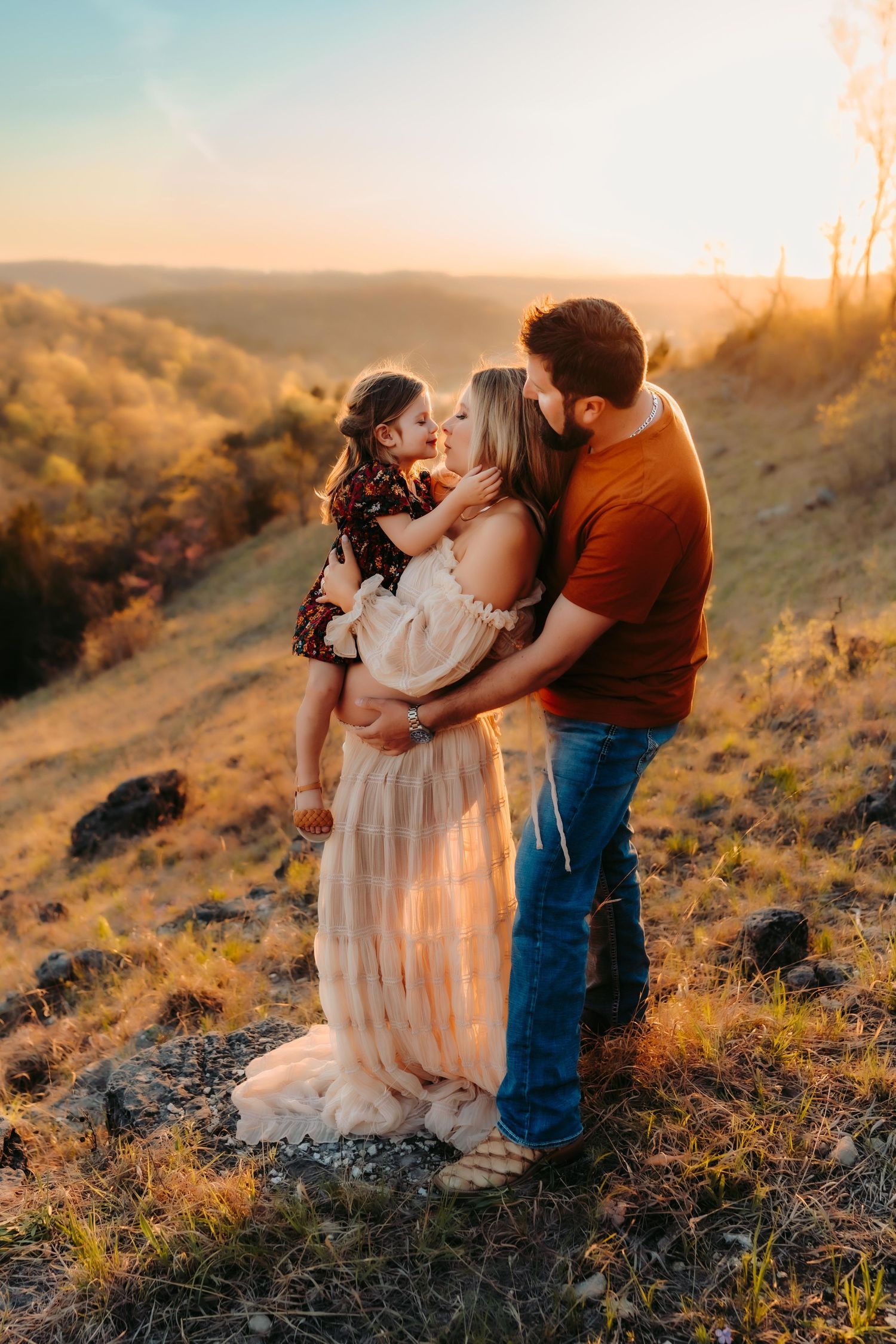 Family embracing on a hillside at sunset, with golden light illuminating the scene.
