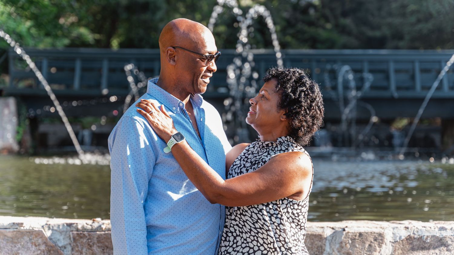 Couple embracing near fountain in outdoor park setting.
