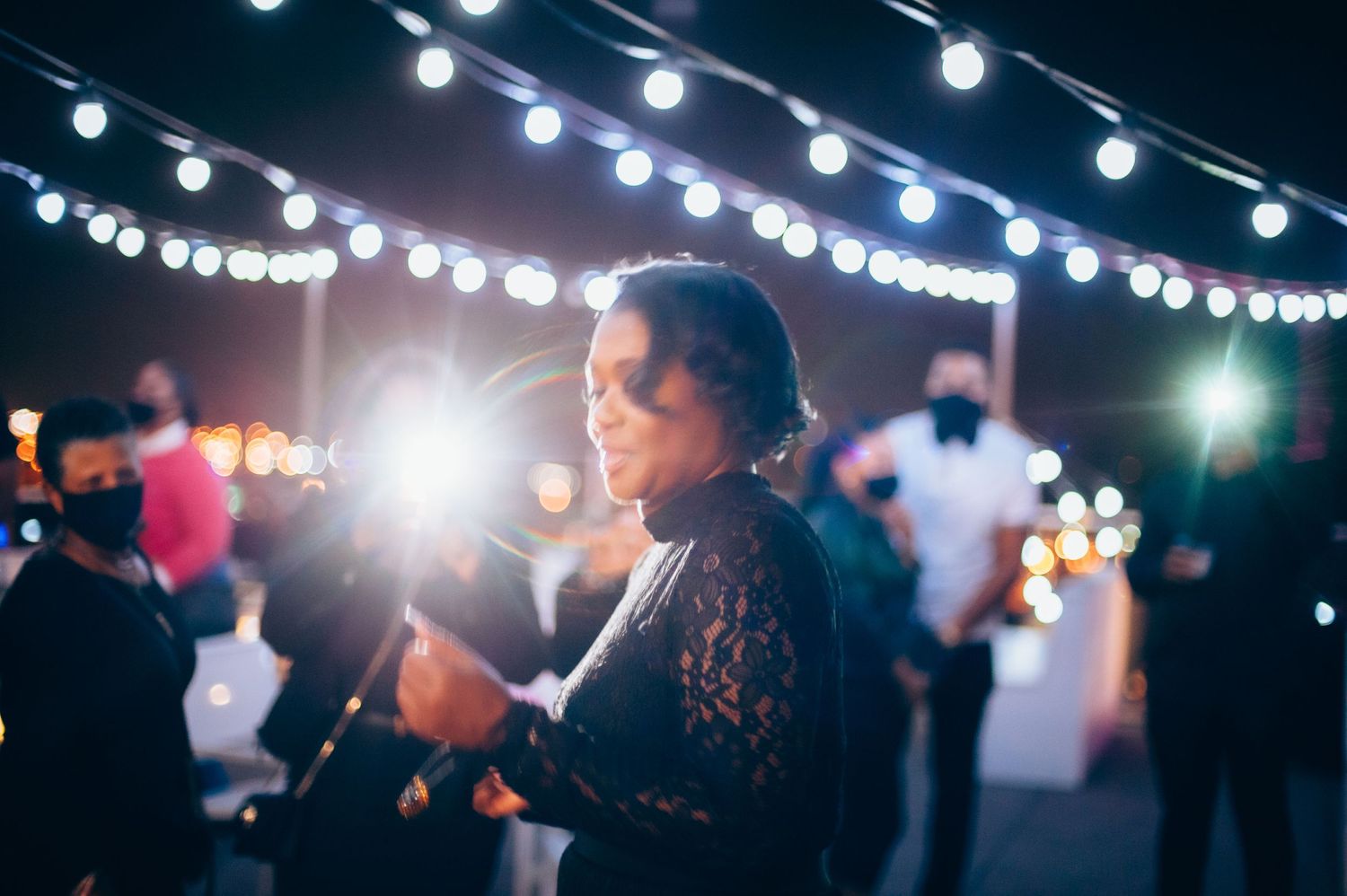 A person enjoying an evening outdoor party under string lights.
