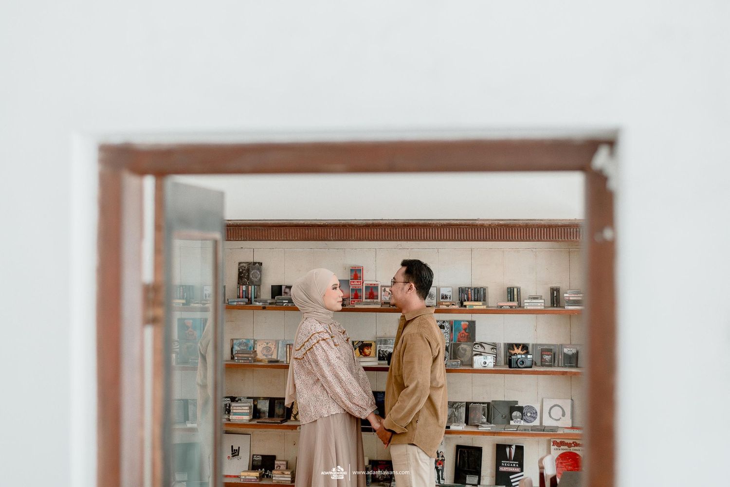 A couple stands together in a room with camera equipment displayed on shelves.