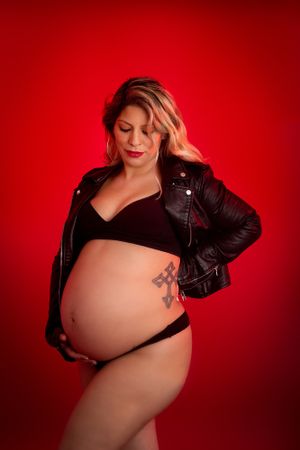 Red Background Maternity Photo of Mama with Black Leather Jacket and Black Bra - Edgy Maternity - Dawn Talia Photography - Port Chester, NY