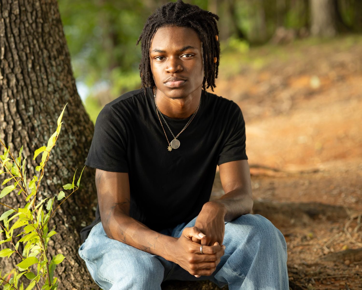 Person sitting against tree trunk wearing black t-shirt and light jeans.