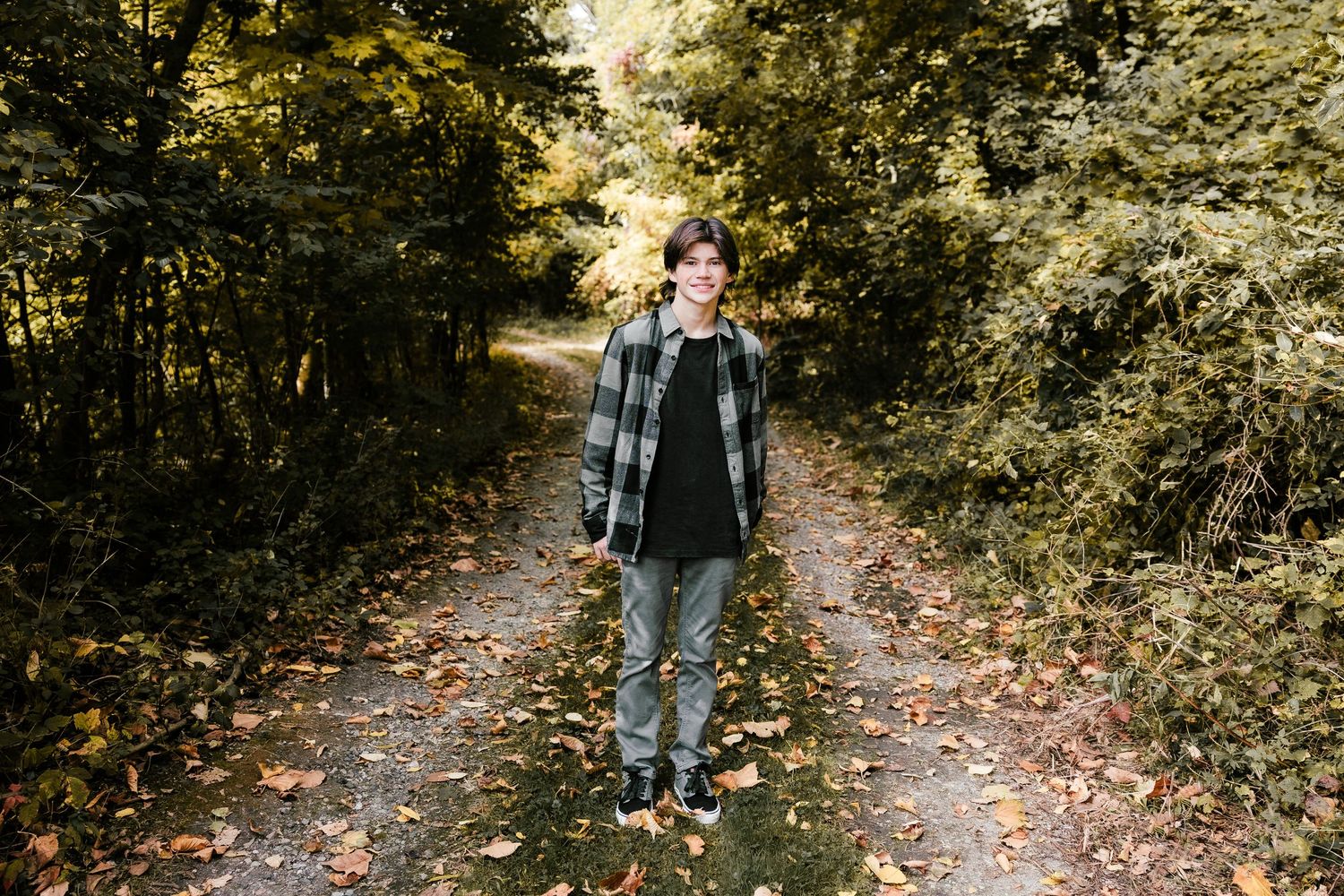 Full length portrait on wooded autumn path wearing plaid shirt and jeans.
