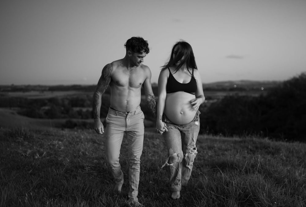 Black and white maternity session showing couple walking through field.