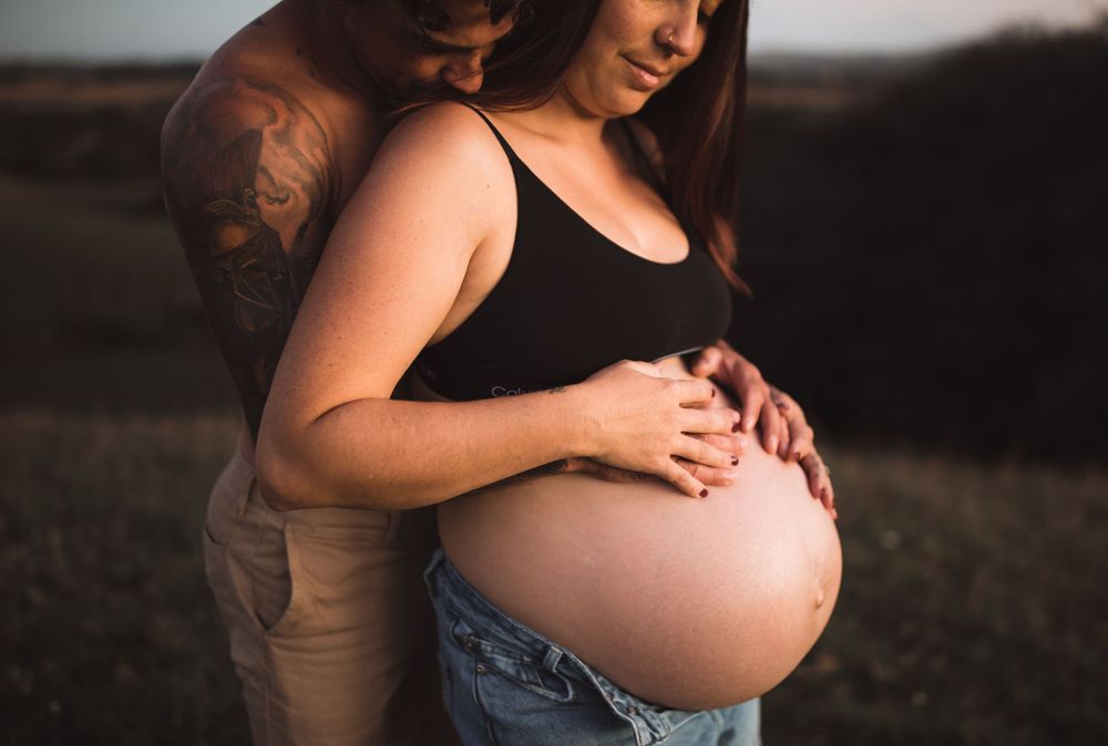 Black and white maternity portrait with couple sharing tender moment outdoors.