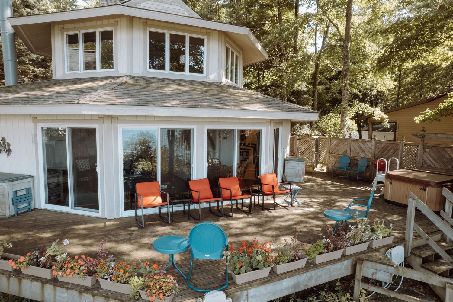 Waterfront cottage with expansive deck featuring colorful outdoor furniture and planters.