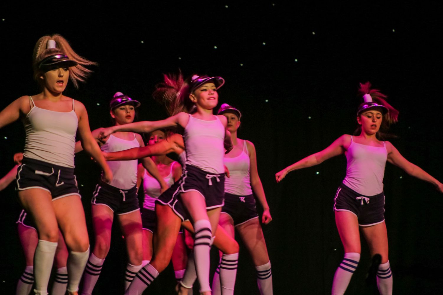 Group of roller derby performers in pink and black outfits dancing on stage during a show.