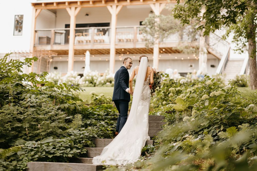 Bride and groom share a romantic moment on garden steps surrounded by lush greenery near a venue.