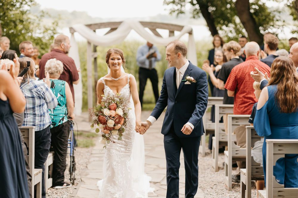 Smiling bride holding bouquet and groom walk hand in hand down the aisle after wedding ceremony.