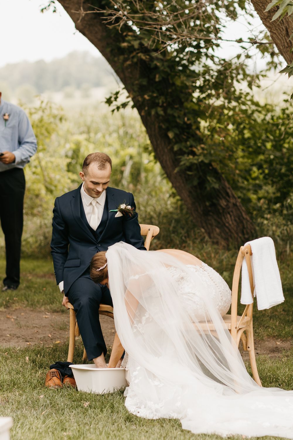 Groom seated outdoors washing bride's feet in a white basin during a meaningful wedding ceremony tradition.