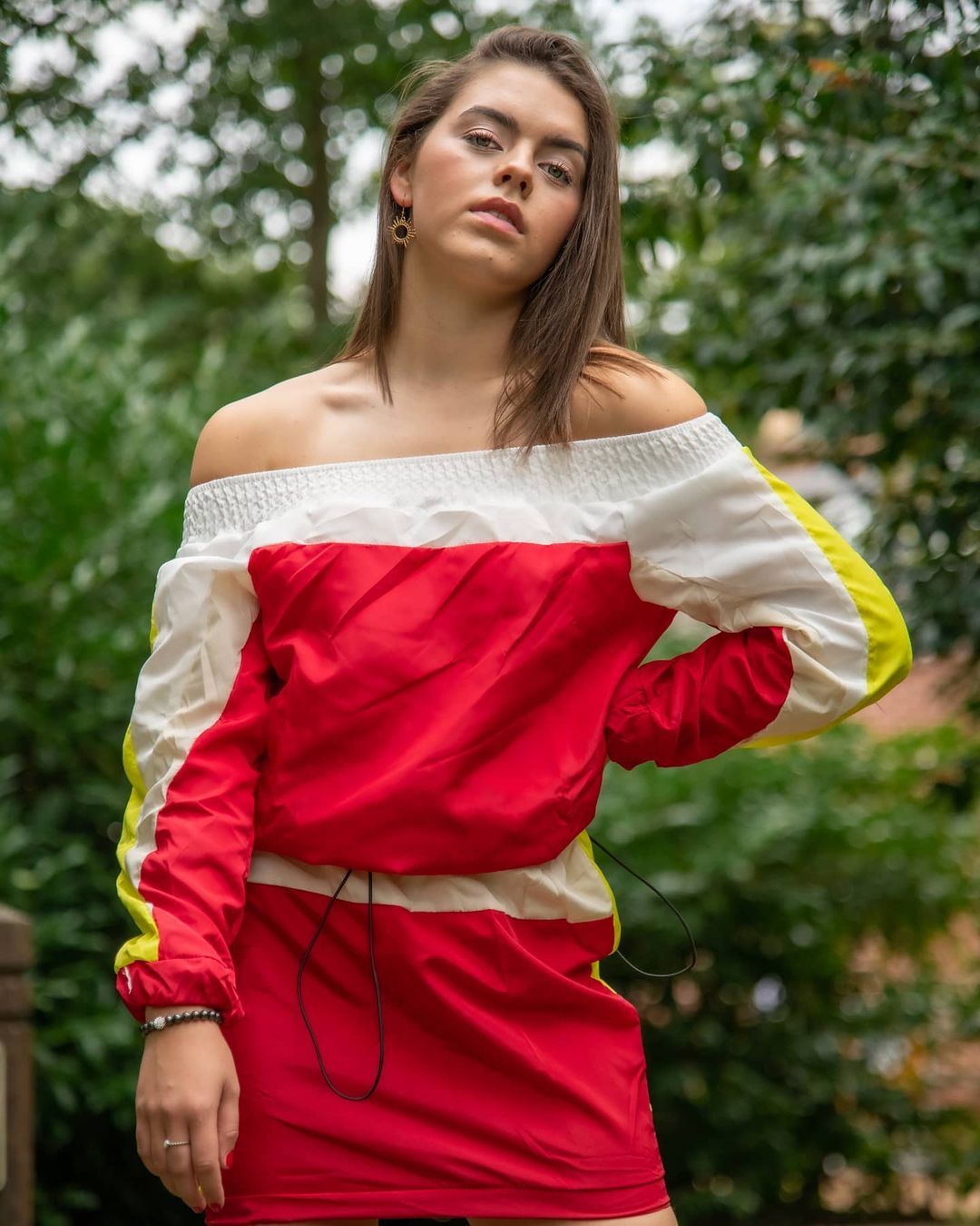 Stylish red and white off-shoulder athletic wear photographed in garden setting.