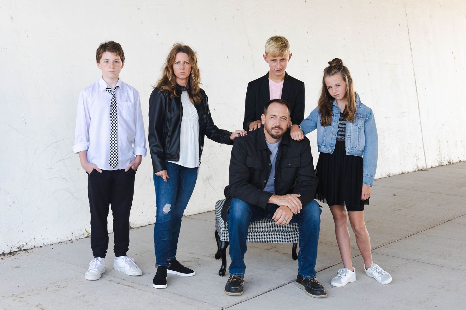 Casual family portrait of five people in mixed casual attire against a white wall background.