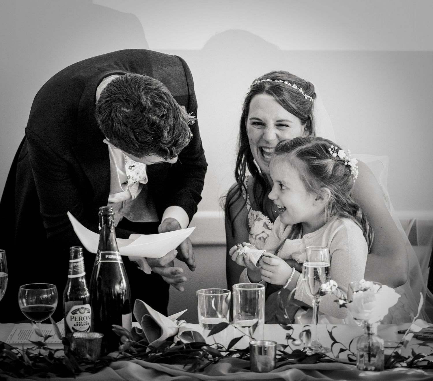 Wedding guests share a joyful moment around a table with champagne and decorations at a reception.