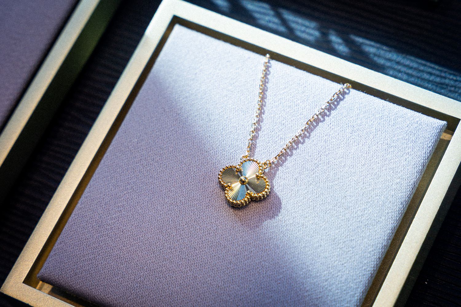 A delicate gold necklace with a small crystal-encrusted pendant displayed on a textured gray surface.