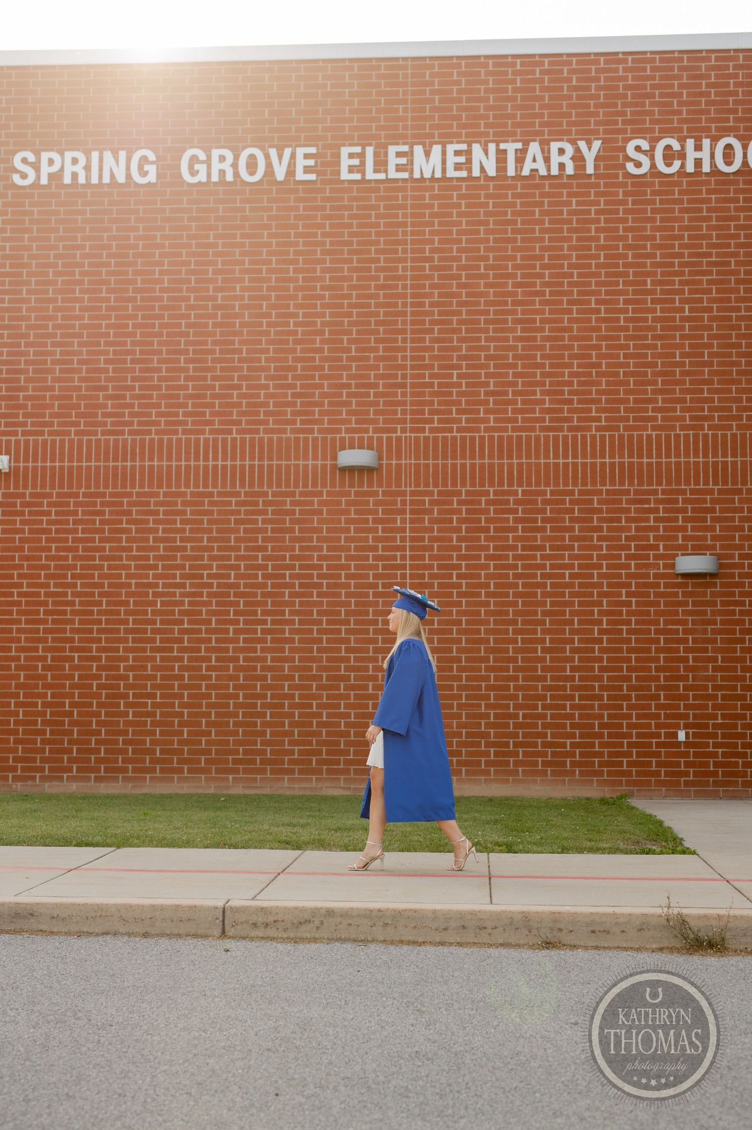 Graduate walks past Spring Grove Elementary School brick wall in blue graduation attire.