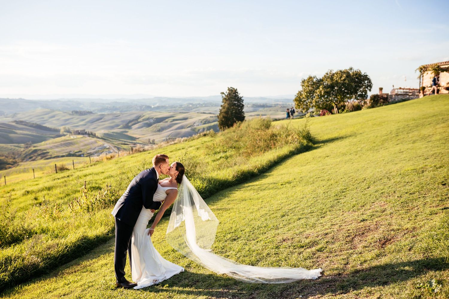 A kiss between a bride and groom while their reception at The Lazy Olive goes on in the background.