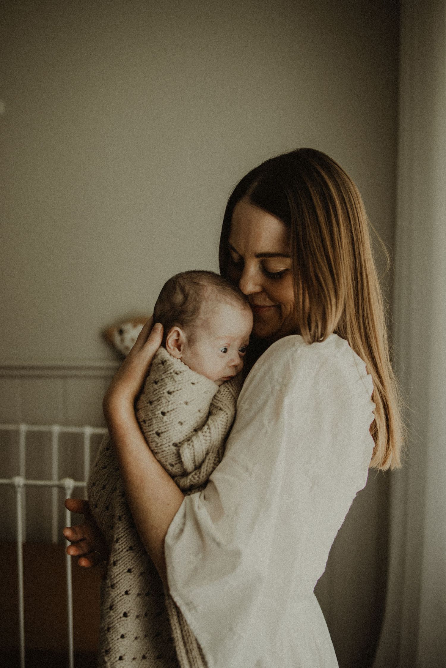A tender moment between parent and infant in soft natural light against a neutral wall.