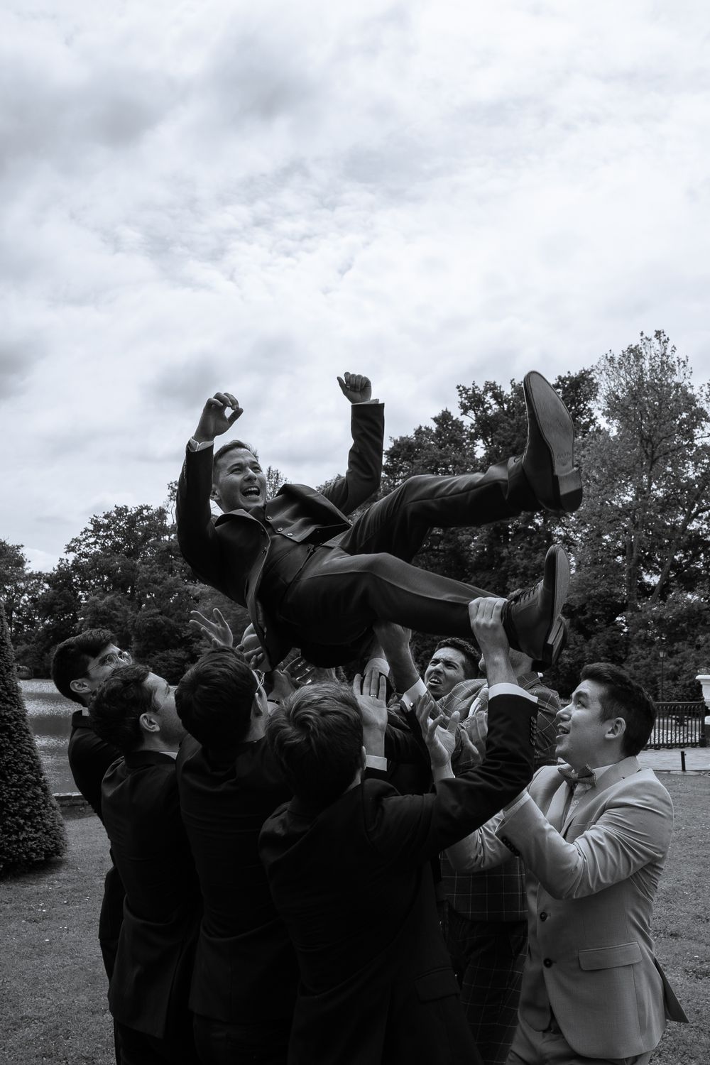 Wedding party groomsmen toss their hats into the air in celebration on a cloudy day.