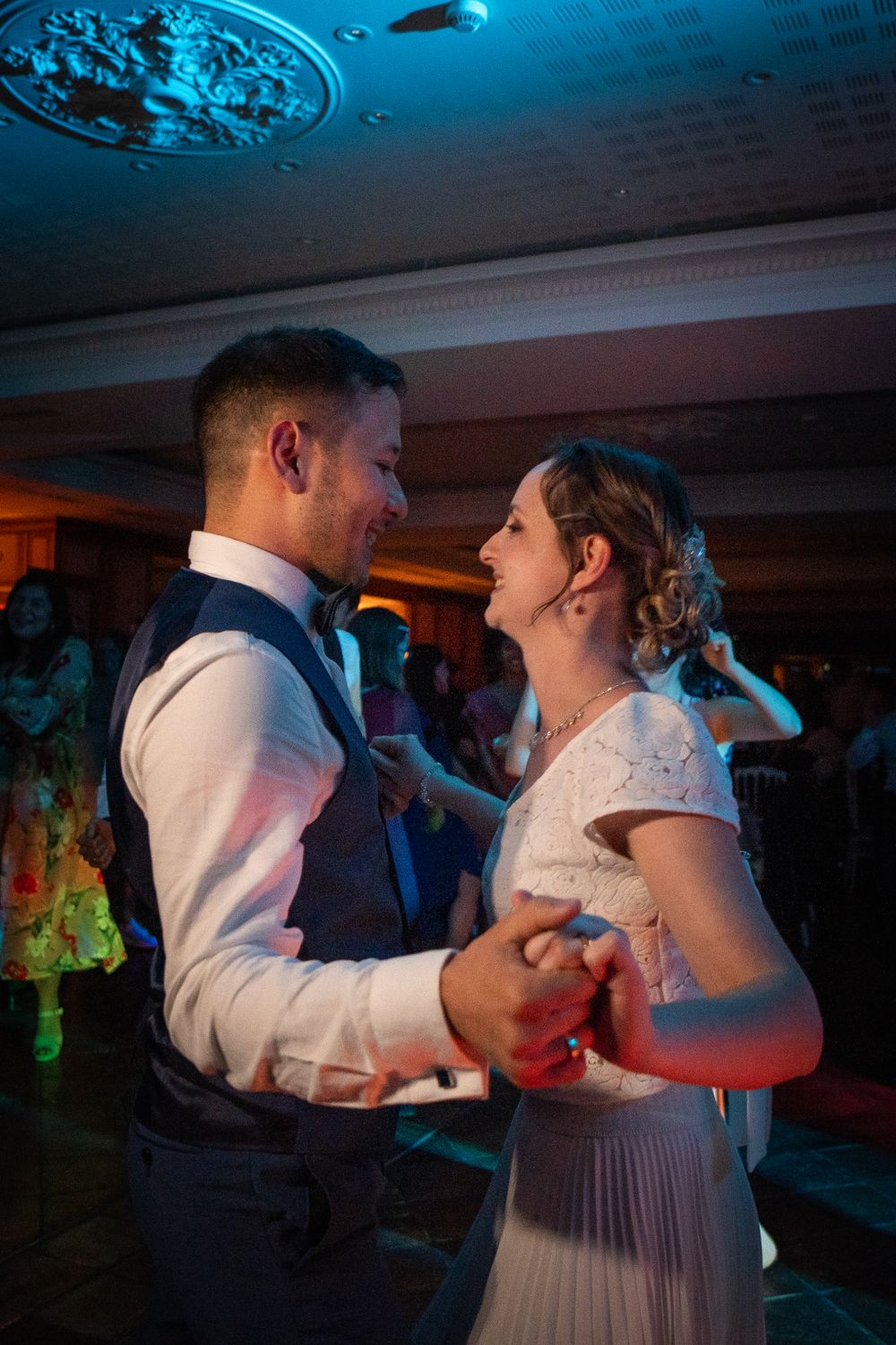 Couple dancing energetically under blue lighting at their wedding reception.