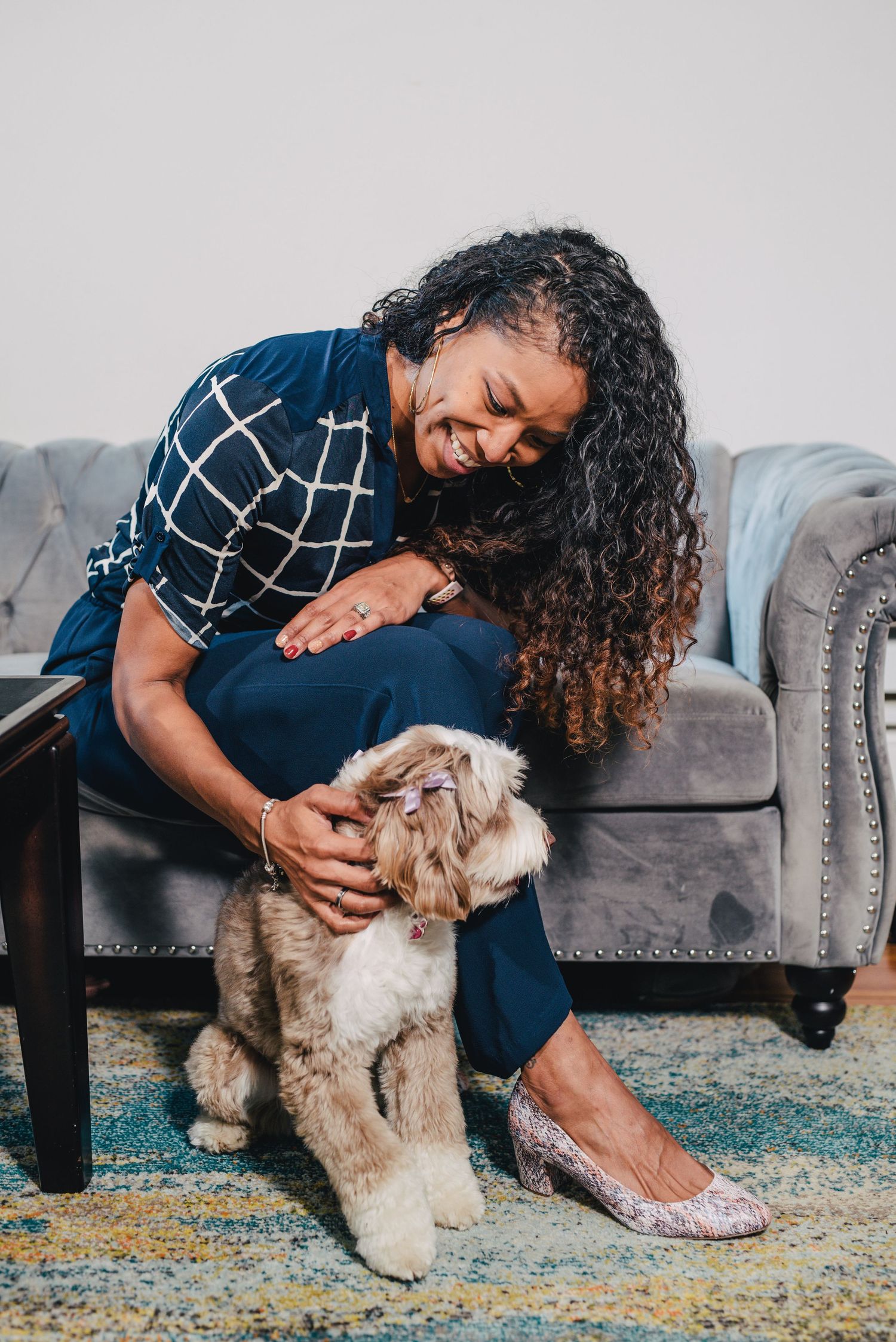 Woman in plaid shirt sharing a joyful moment with her small fluffy dog on a gray couch.
