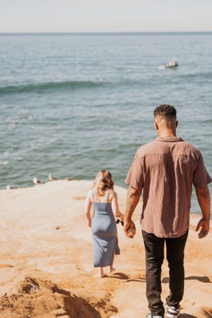 Two people walking together on a sandy beach by the ocean.