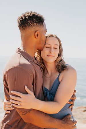 Couple embracing on a sunny beach with the ocean in the background.