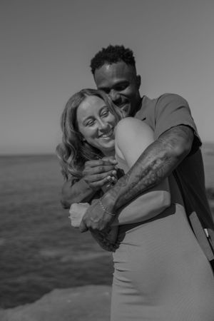 Intimate black and white photo of a couple embracing by the sea.