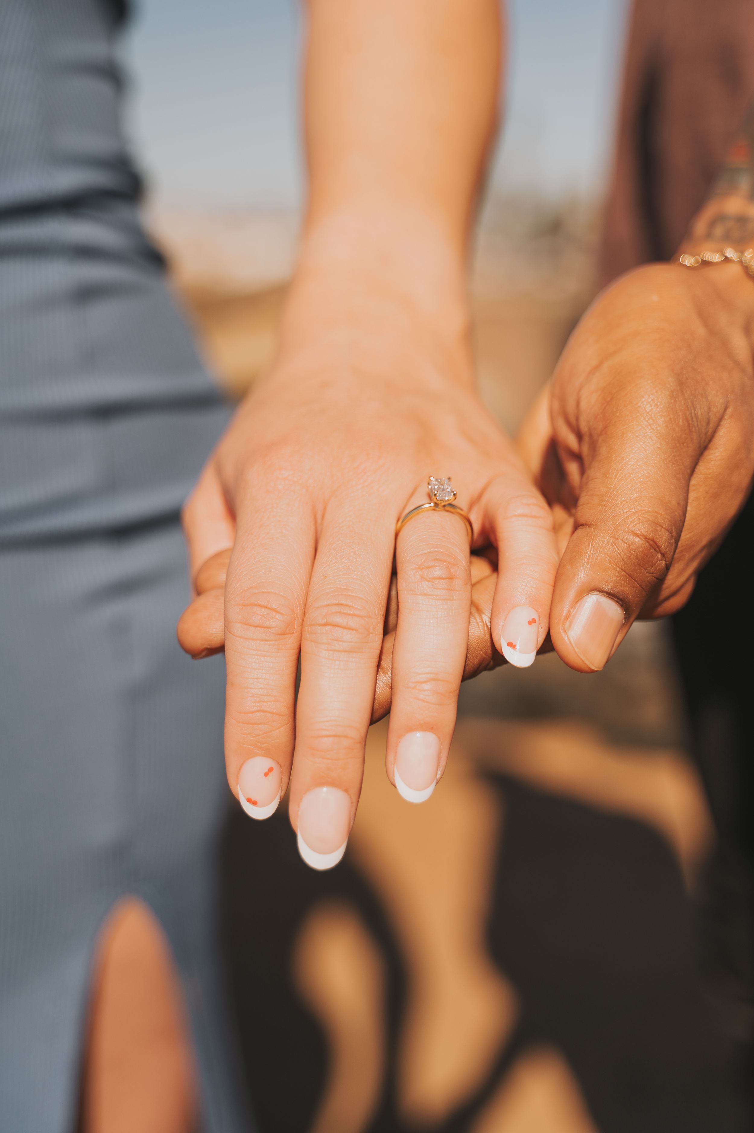 Close-up of hands showing an engagement ring with French manicure.