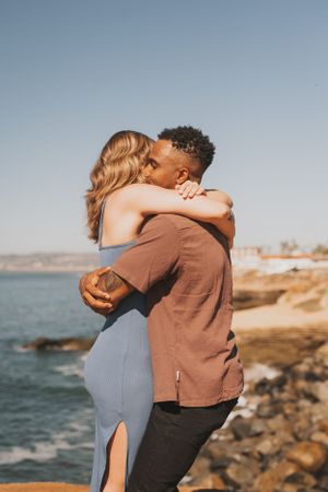Romantic embrace on a cliff overlooking the ocean during sunset.