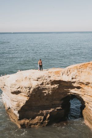 Natural rock arch formation on a beach with ocean waves and blue sky.