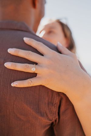 Close-up shot of hands against a wooden surface showing an engagement ring.