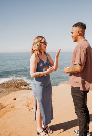 Two people share an emotional exchange on a scenic cliff overlooking the ocean.