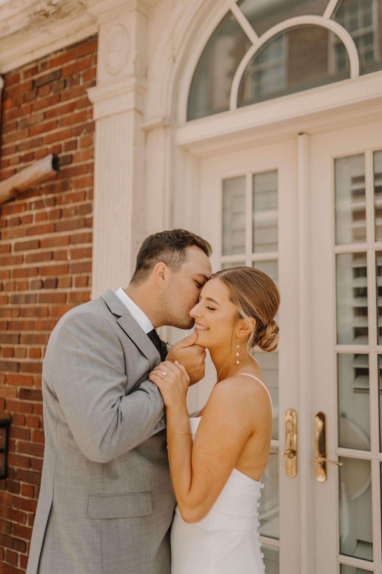 Intimate wedding moment shared between couple against brick building with white trim.