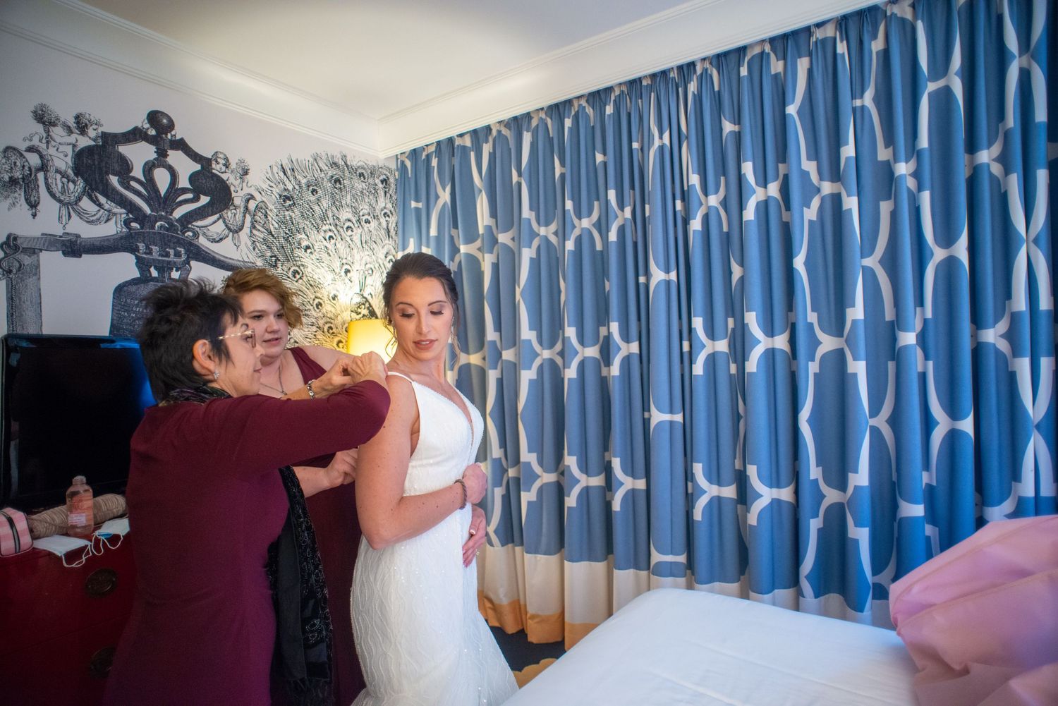 Getting ready scene with bride being helped with wedding dress preparations.
