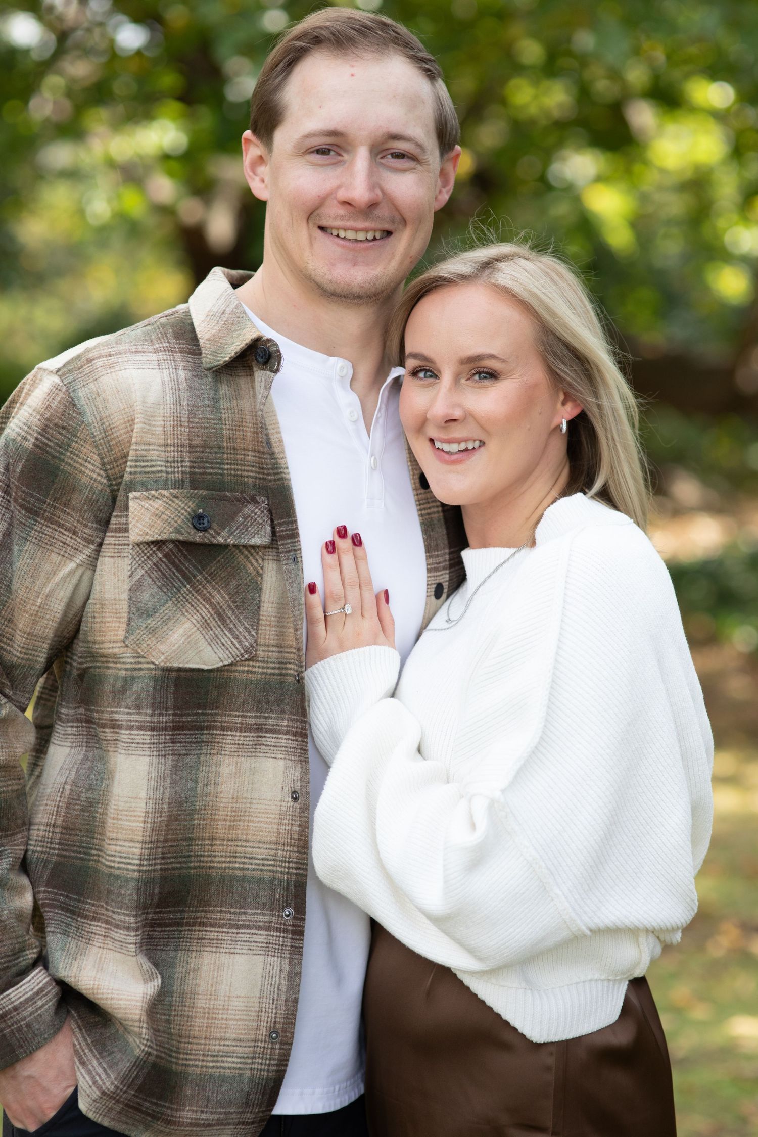 A couple in casual fall attire poses together outdoors on an autumn day.