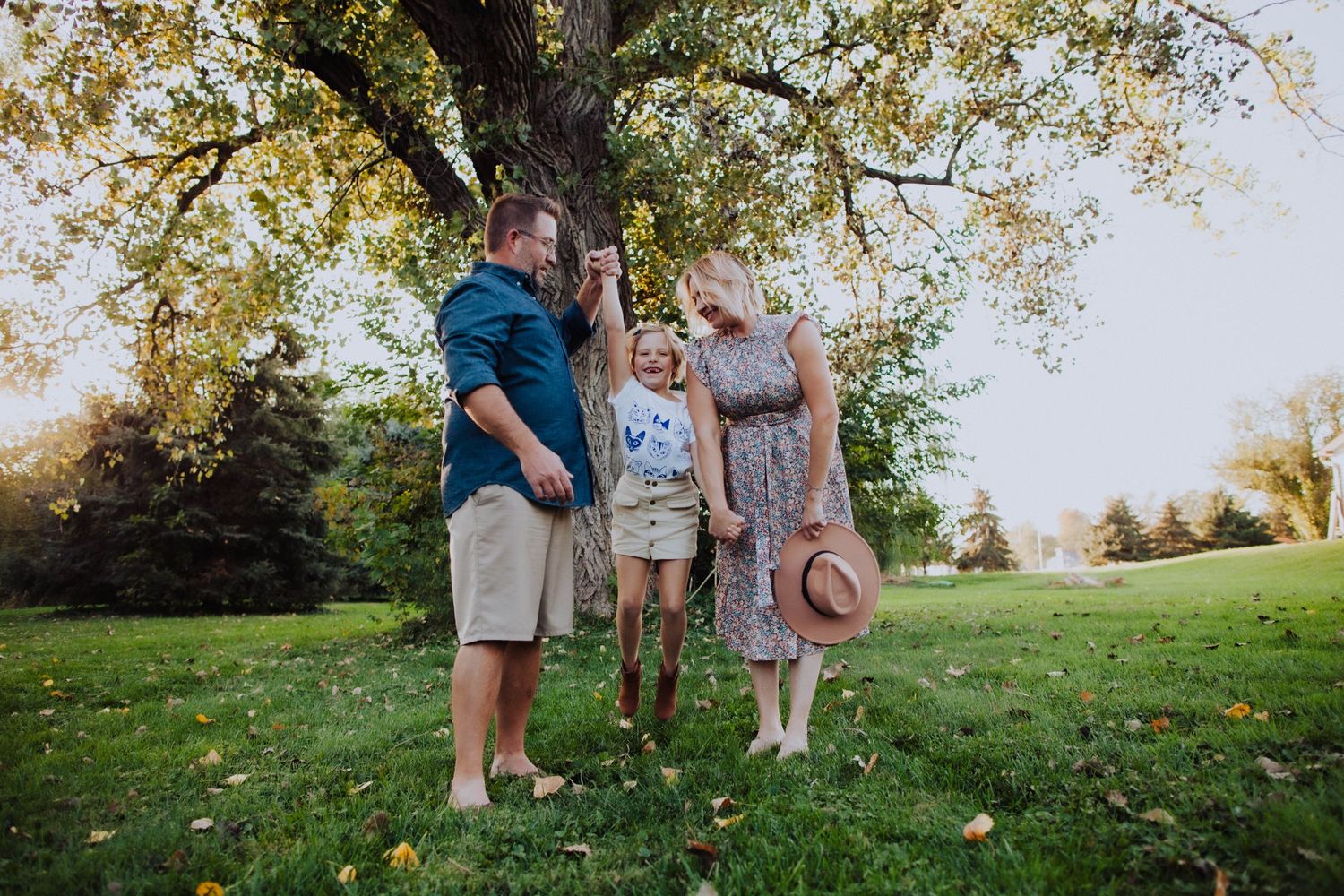 A family group stands beneath a large tree in a sunny park setting.