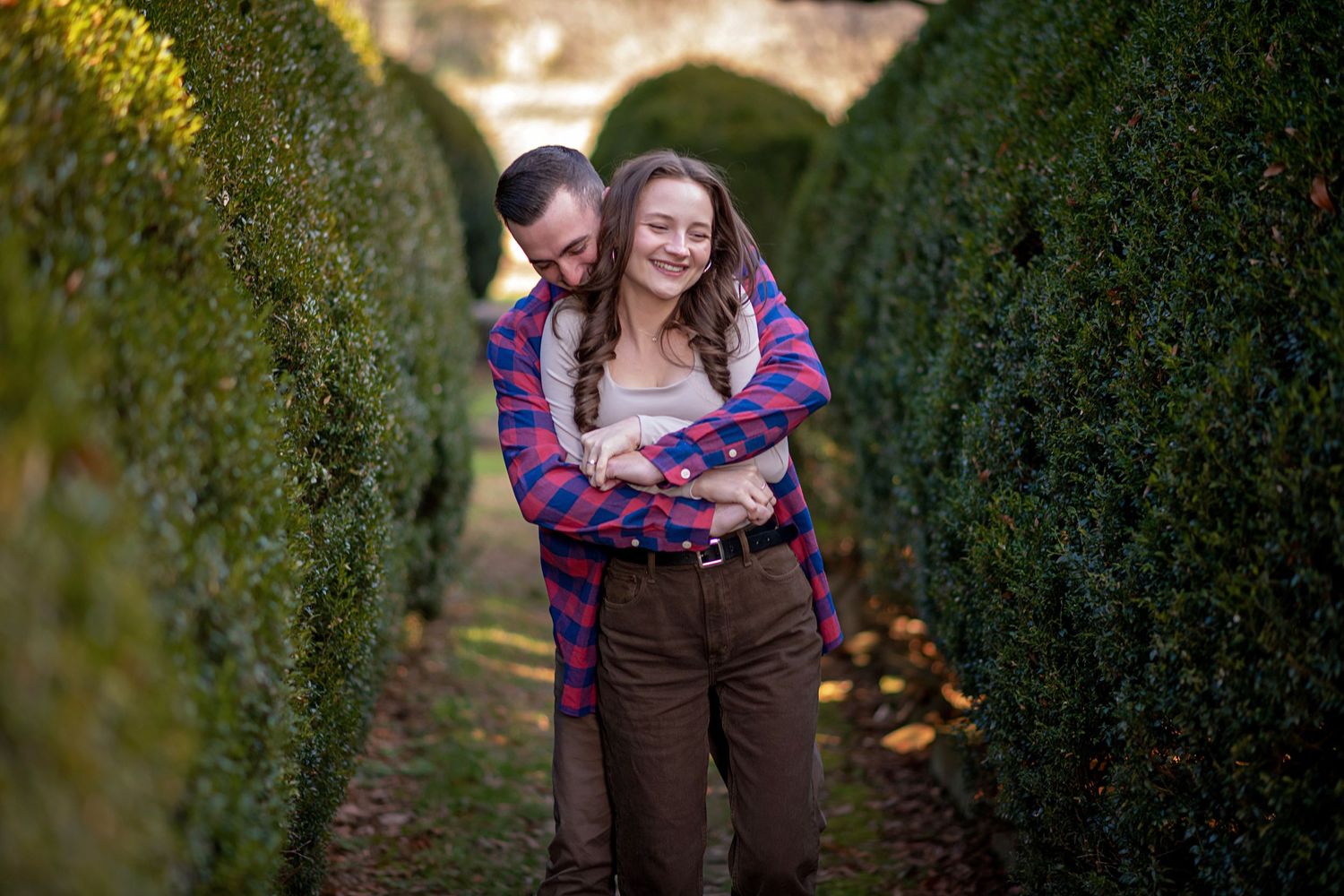 Couple sharing romantic moment between hedgerows in garden setting.