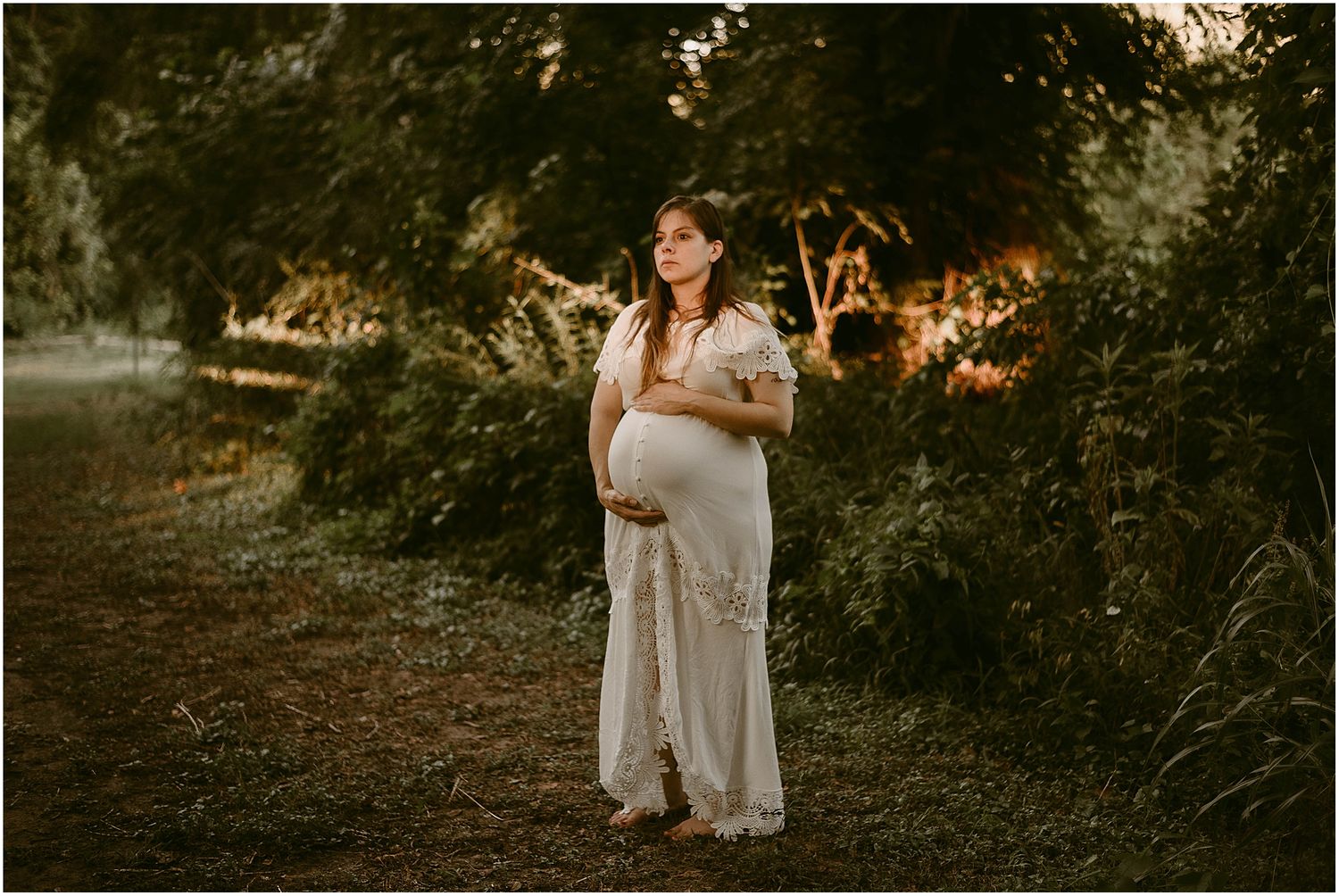 Golden hour maternity portrait in a wooded area with warm sunset lighting.