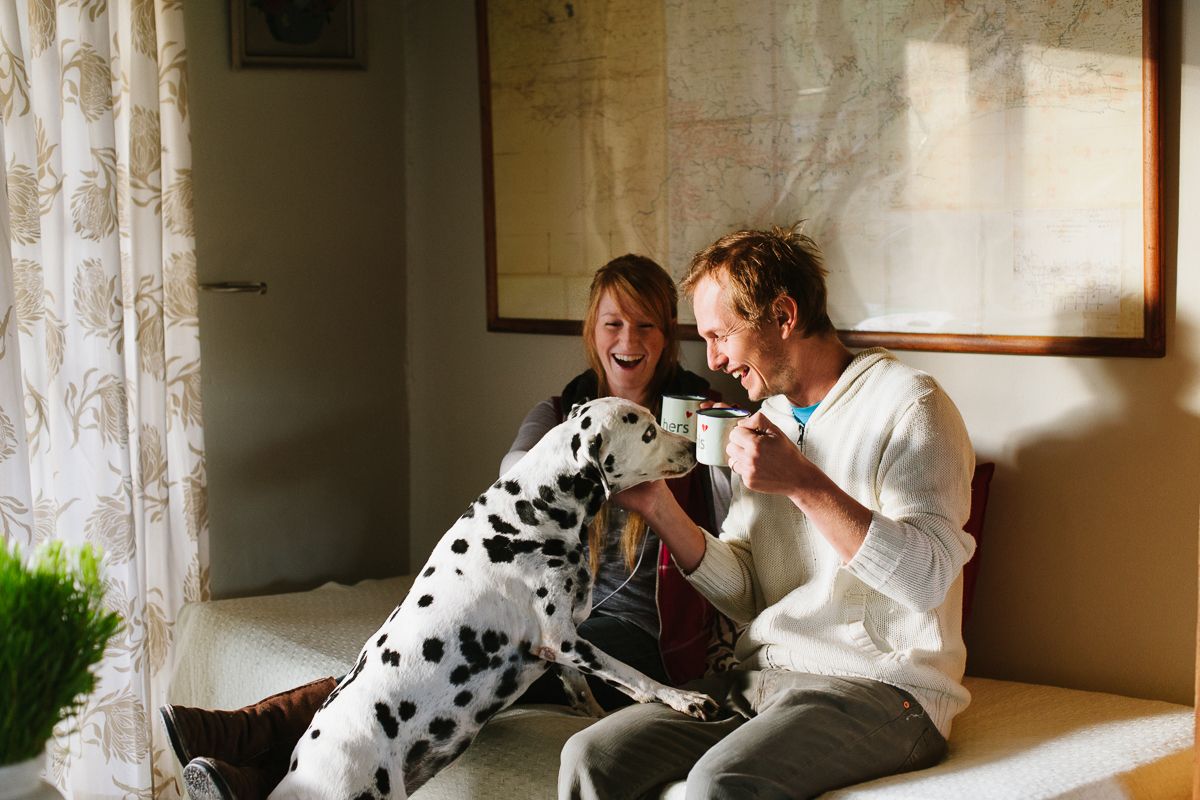 A couple drinks coffee on a couch with their Dalmatian dog.