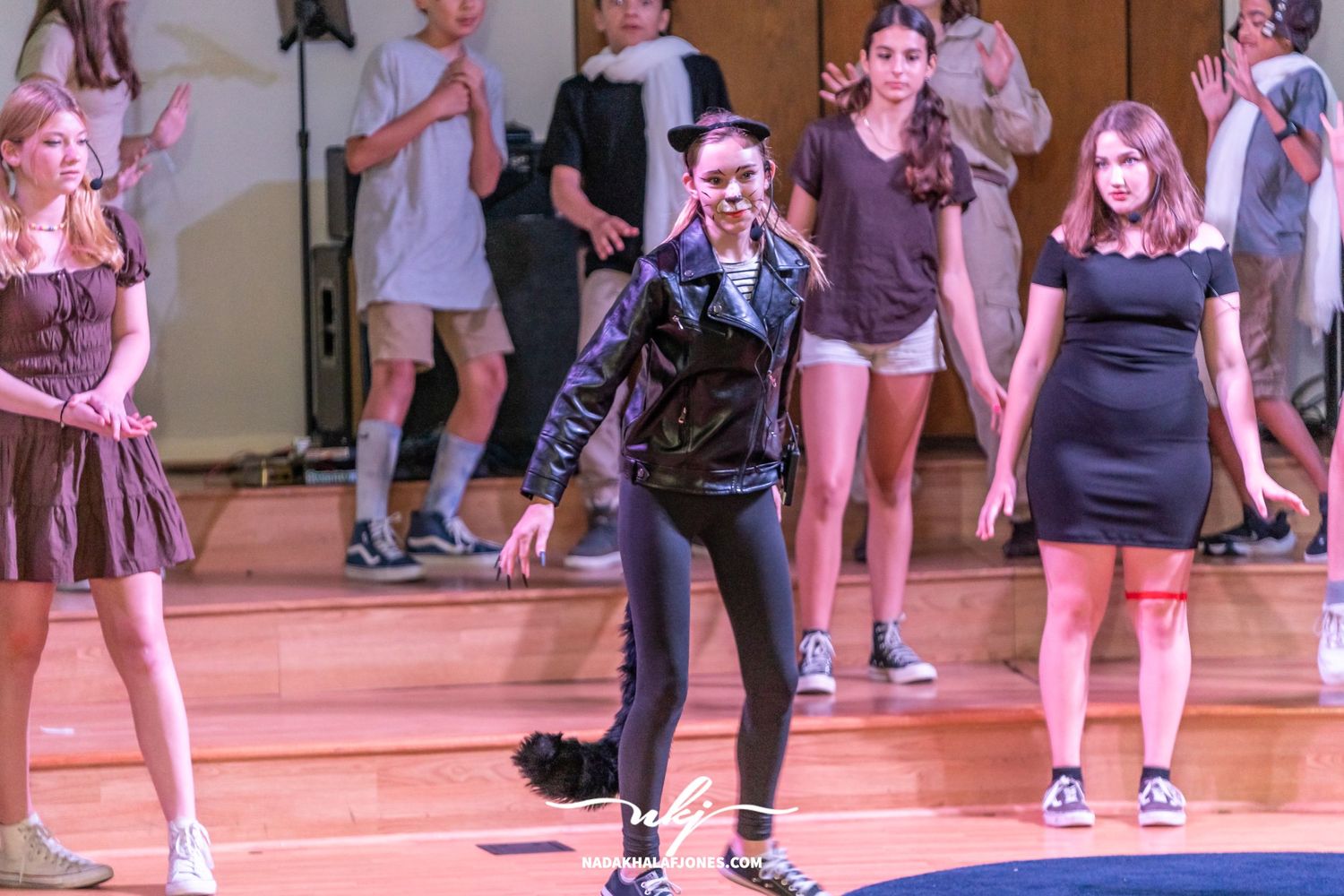 Musical theater performance with performers in dark costumes on a wooden stage.