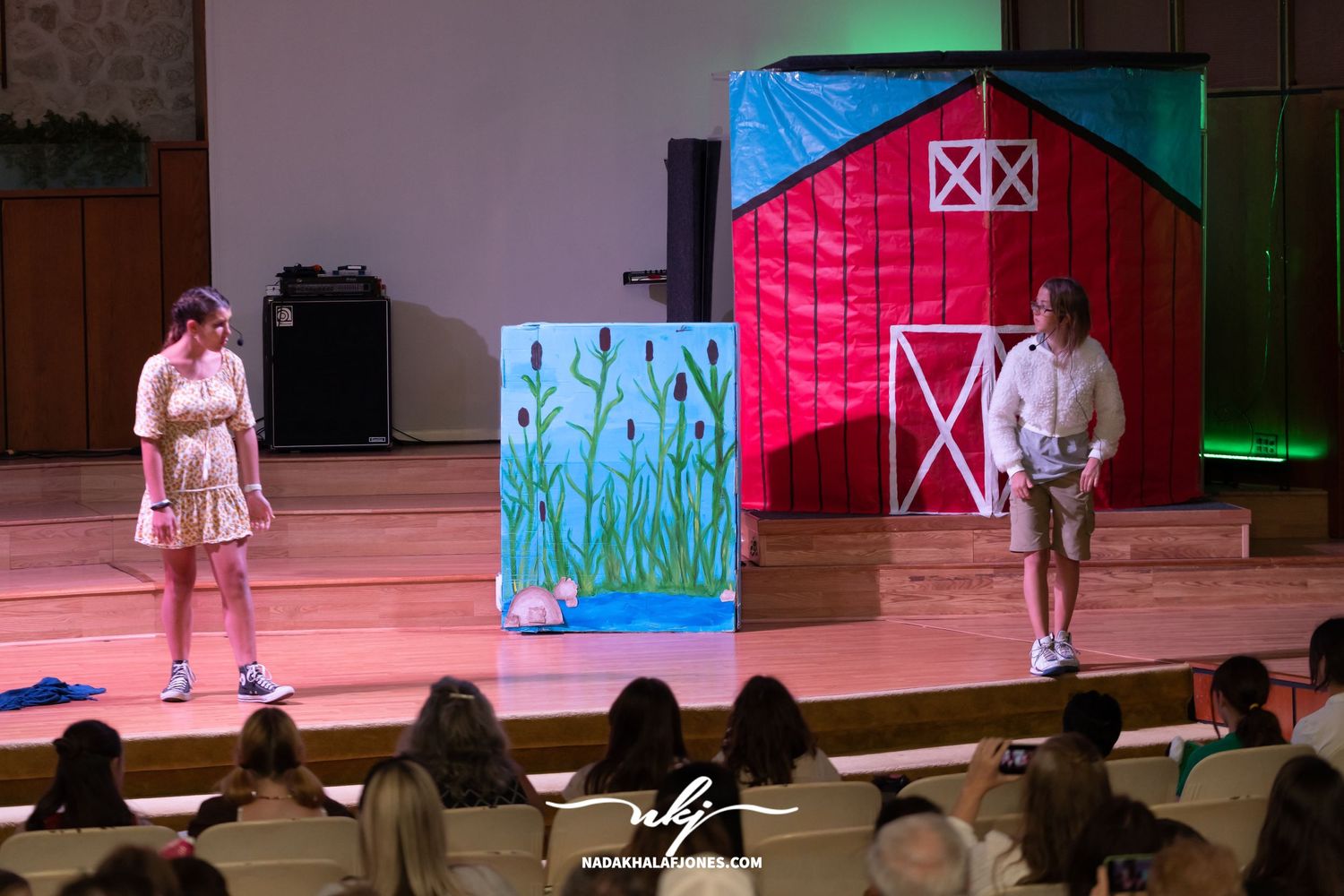 Theater stage with red barn backdrop and performers executing choreographed movements.