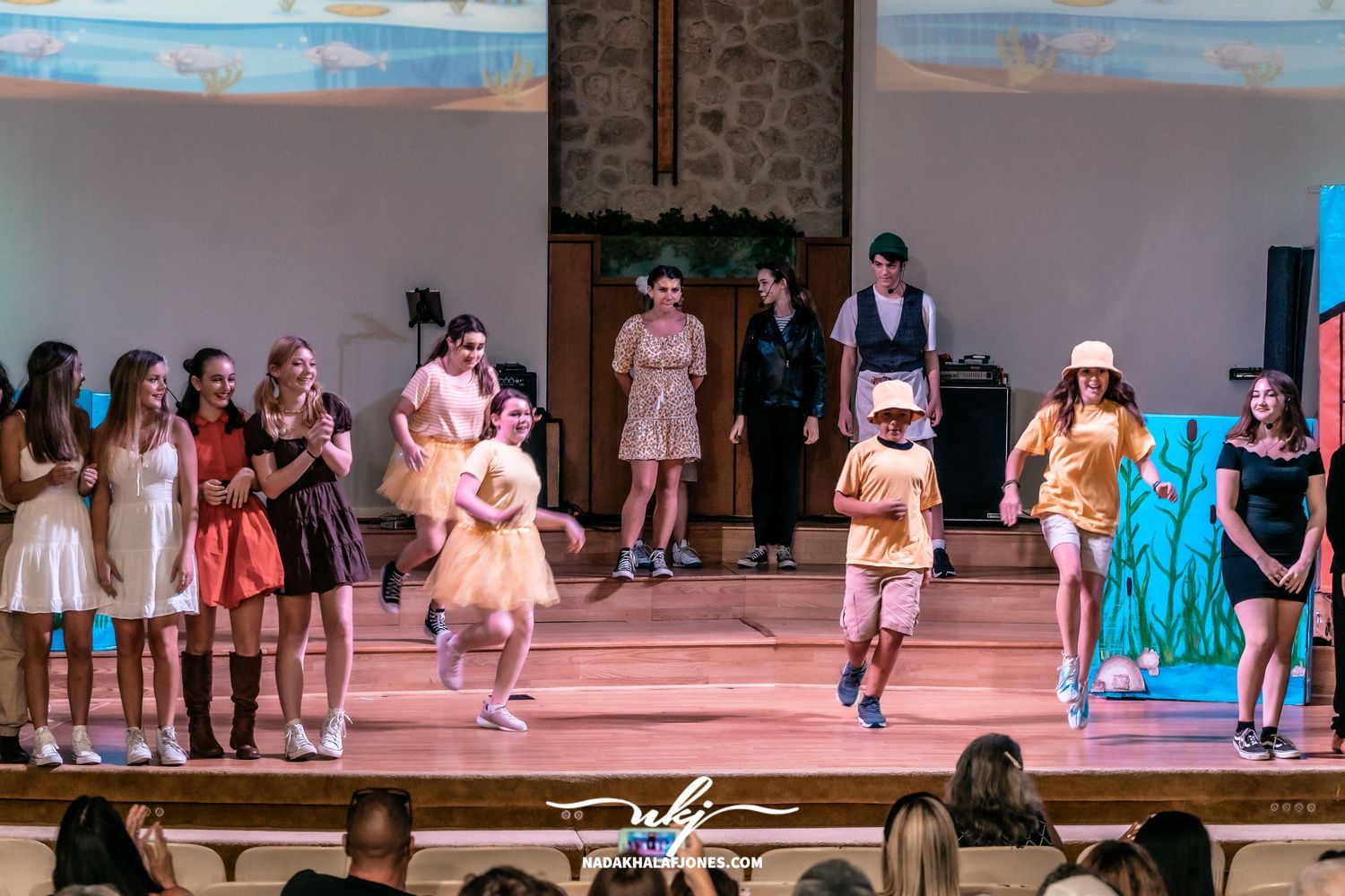 Stage performers in bright costumes line up during a theatrical production number.