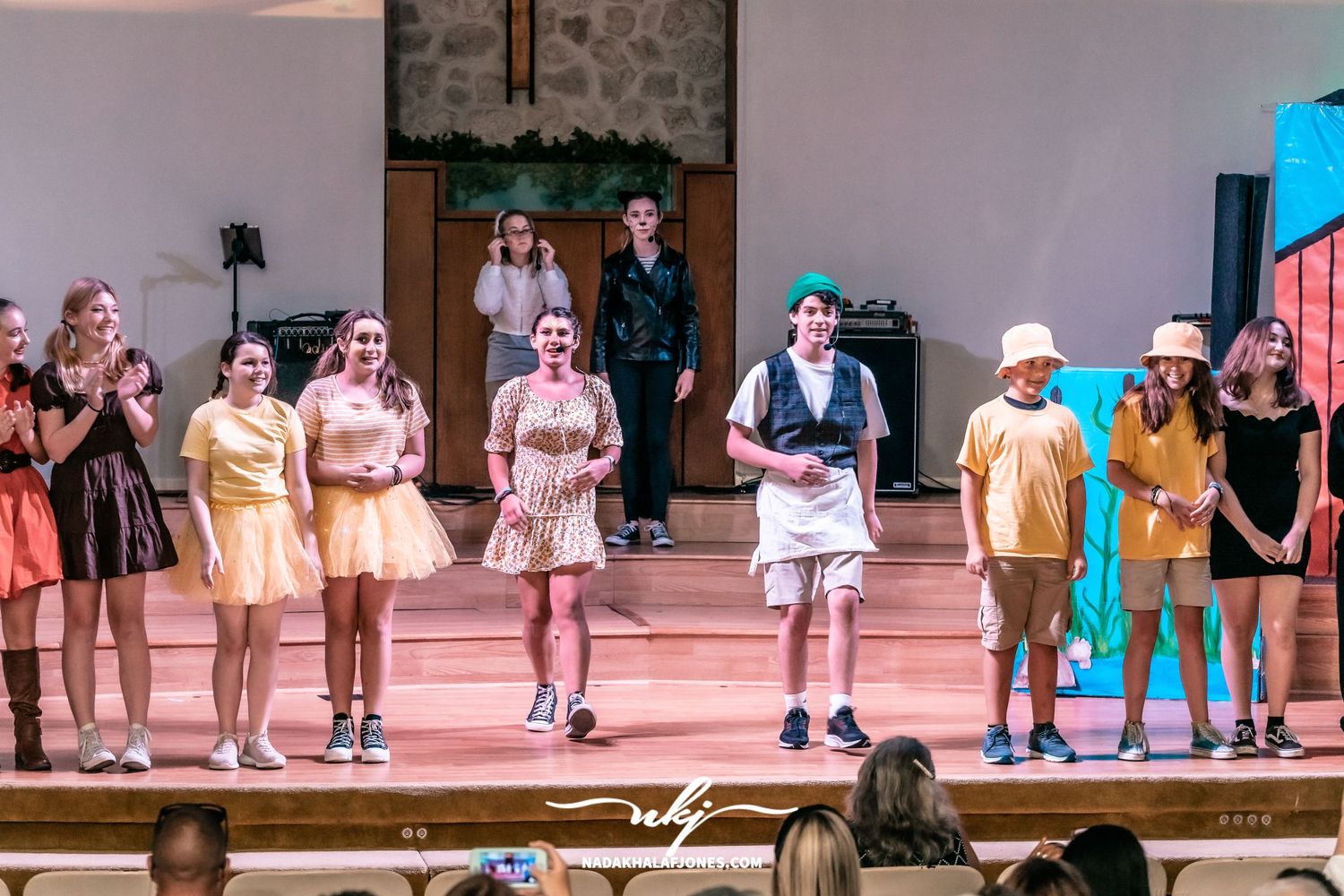 Cast members spread across a theater stage during a performance.
