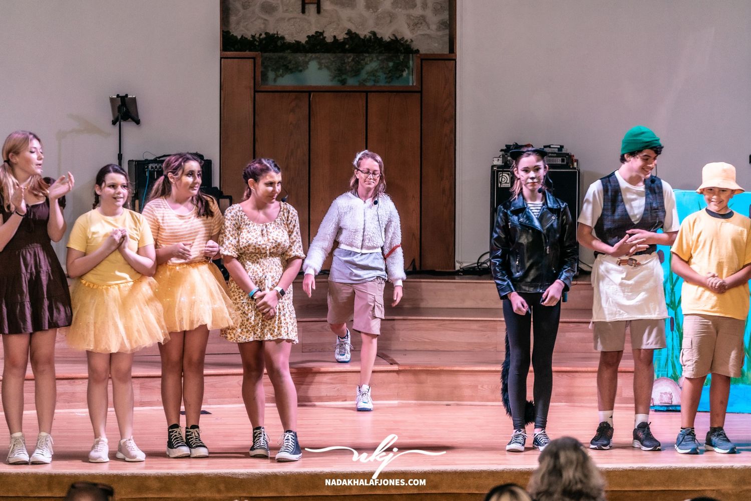 Theater ensemble performs choreographed scene on illuminated stage.