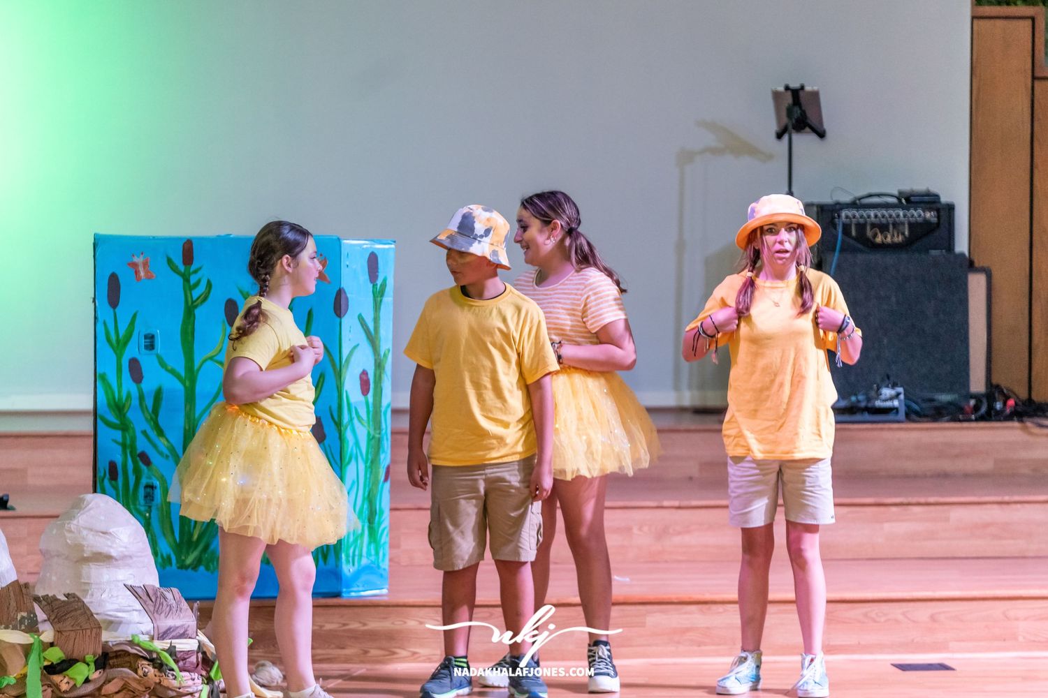 Stage performers act out a colorful scene with painted backdrops and coordinated costumes during a theatrical production.